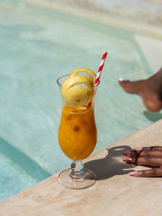 The photo shows a refreshing tropical cocktail placed by the edge of a swimming pool. The drink is served in an elegant glass, decorated with a scoop of ice cream and a colorful straw.