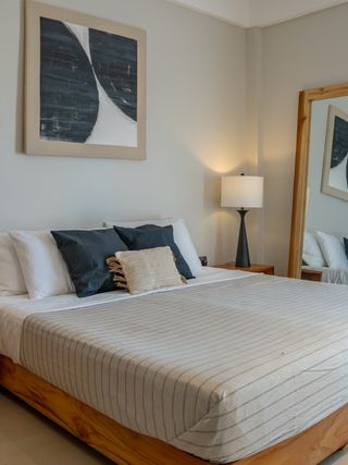 The photo shows an elegant and spacious bedroom designed in a modern, minimalist style. A large bed with a wooden frame is surrounded by bedside tables with lamps, while the light interior colors create a cozy atmosphere.